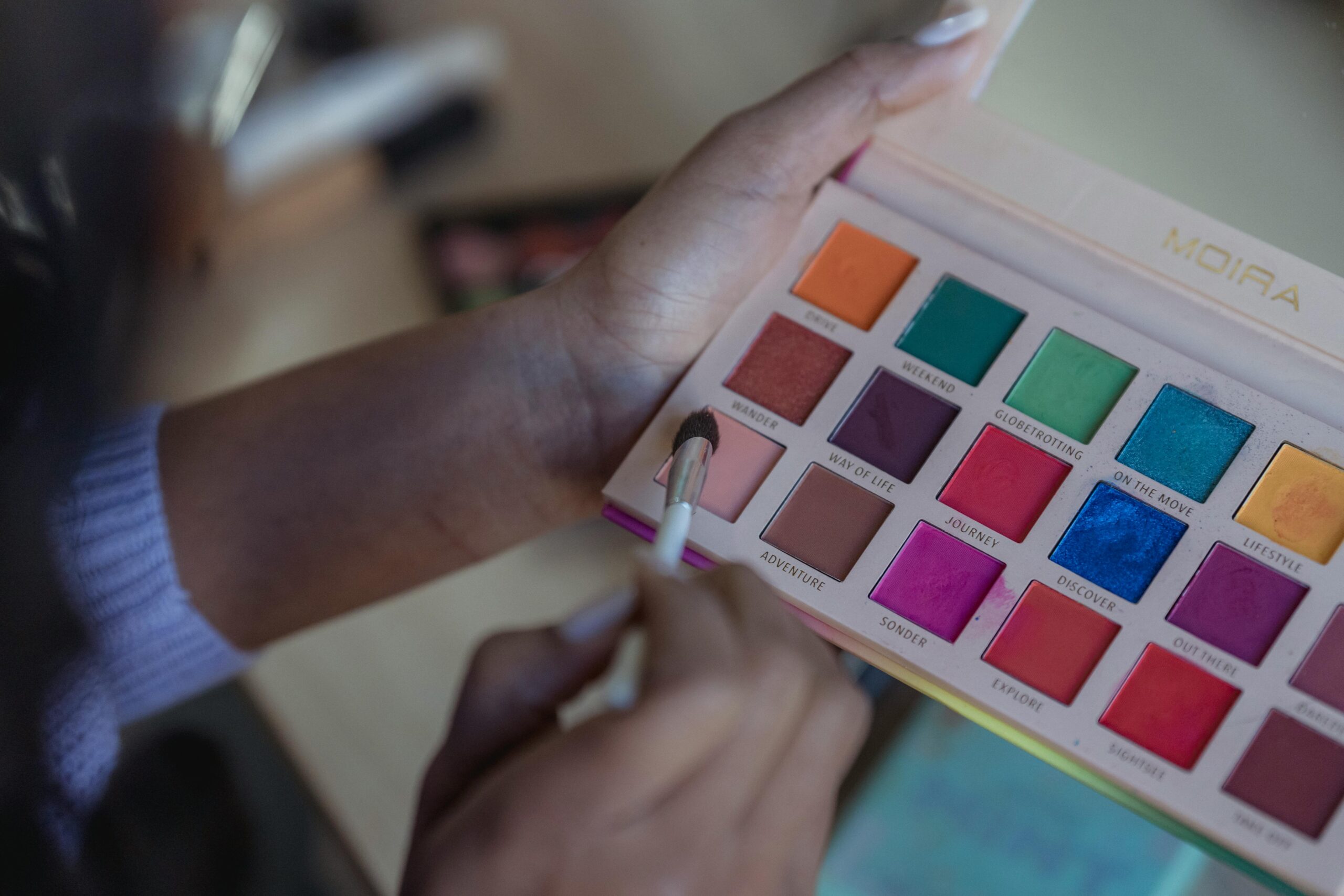 From above of crop anonymous African American female taking bright eyeshadows on brush on blurred background